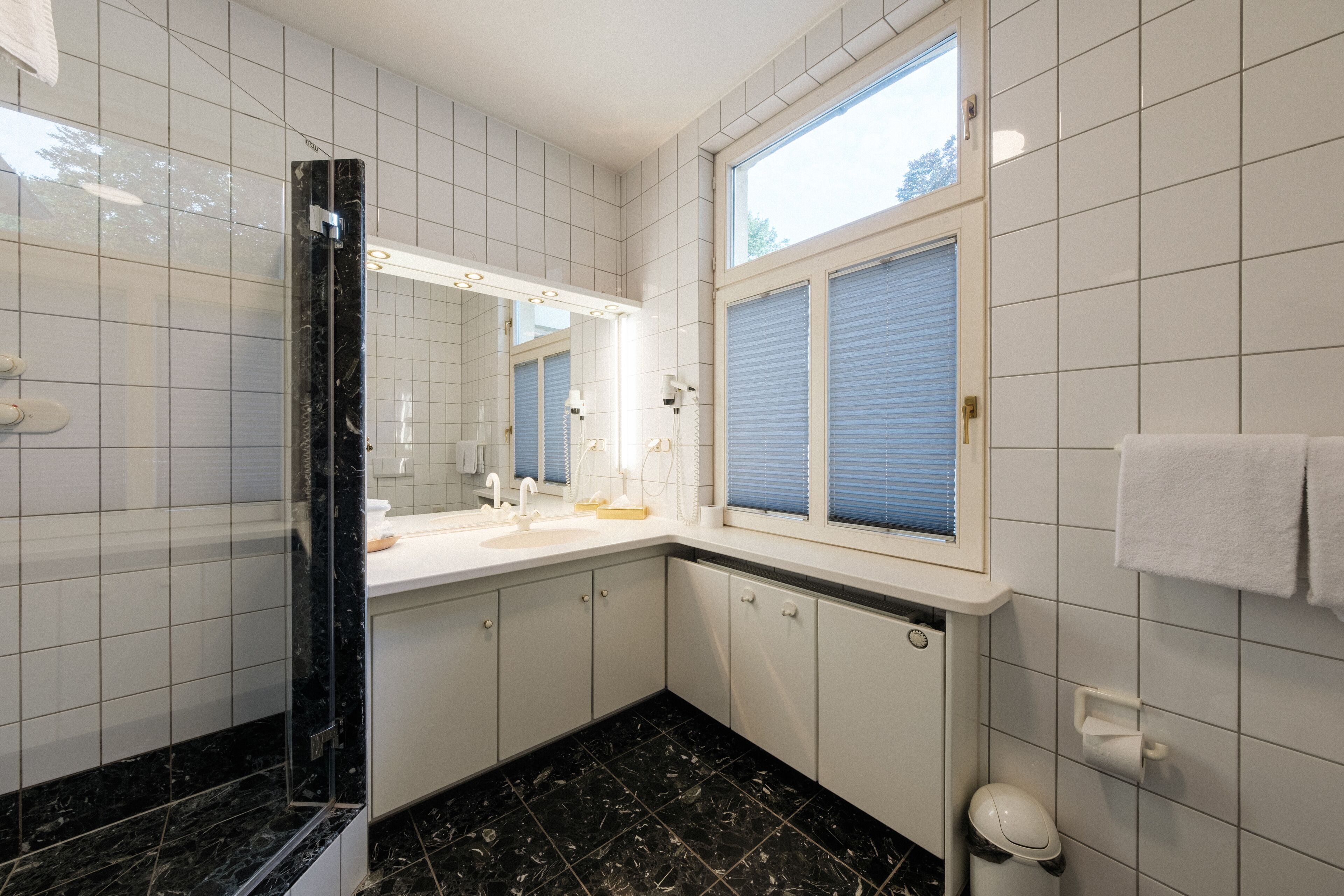 A modern bathroom with a large mirror, a shower, a toilet, and a sink.