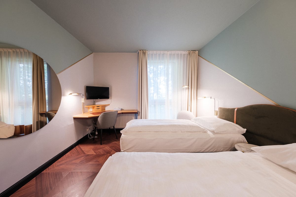 Ein Hotelzimmer mit zwei Betten, einem Schreibtisch, einem Stuhl, einem Fernseher und einem großen Spiegel.