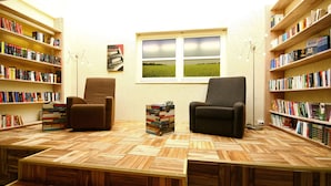 A cozy reading area with two armchairs, a wooden floor, and bookshelves filled with books. - Hotel Haus Duden (Wesel)