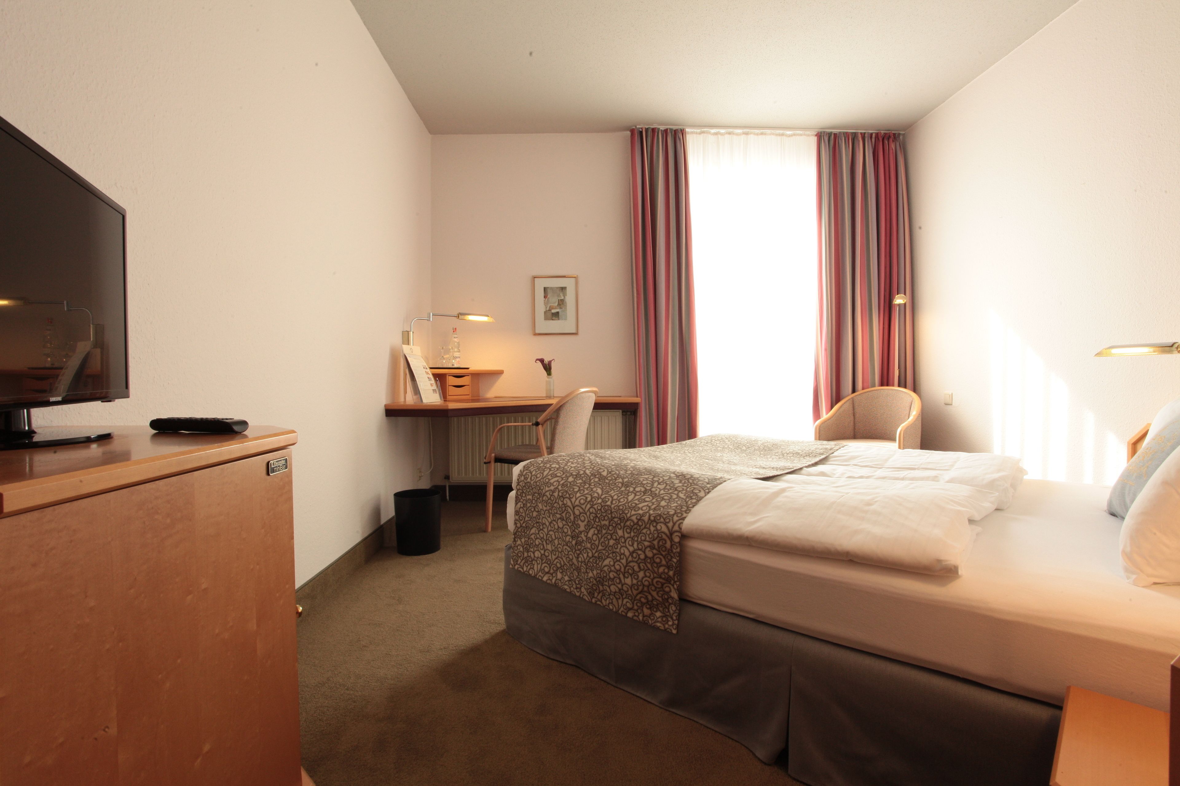 A hotel room with a bed, desk, chair, television, and a window with curtains.