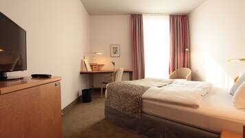 A hotel room with a bed, desk, chair, television, and a window with curtains.
