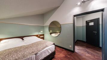Ein Hotelzimmer mit einem Bett, einem runden Spiegel an der Wand, einer Tür und einem Holzboden.