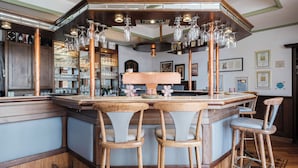 A bar area with wooden stools, copper bar counter, and hanging glassware. - Hotel Haus Duden (Wesel)