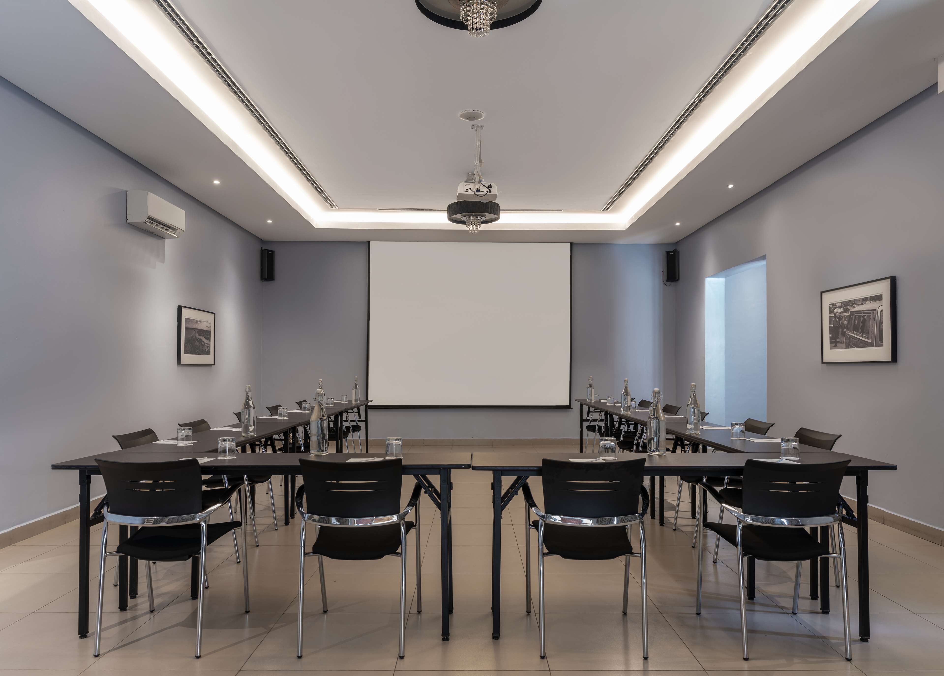 A conference room with a long table, chairs, a projector screen, and a chandelier.