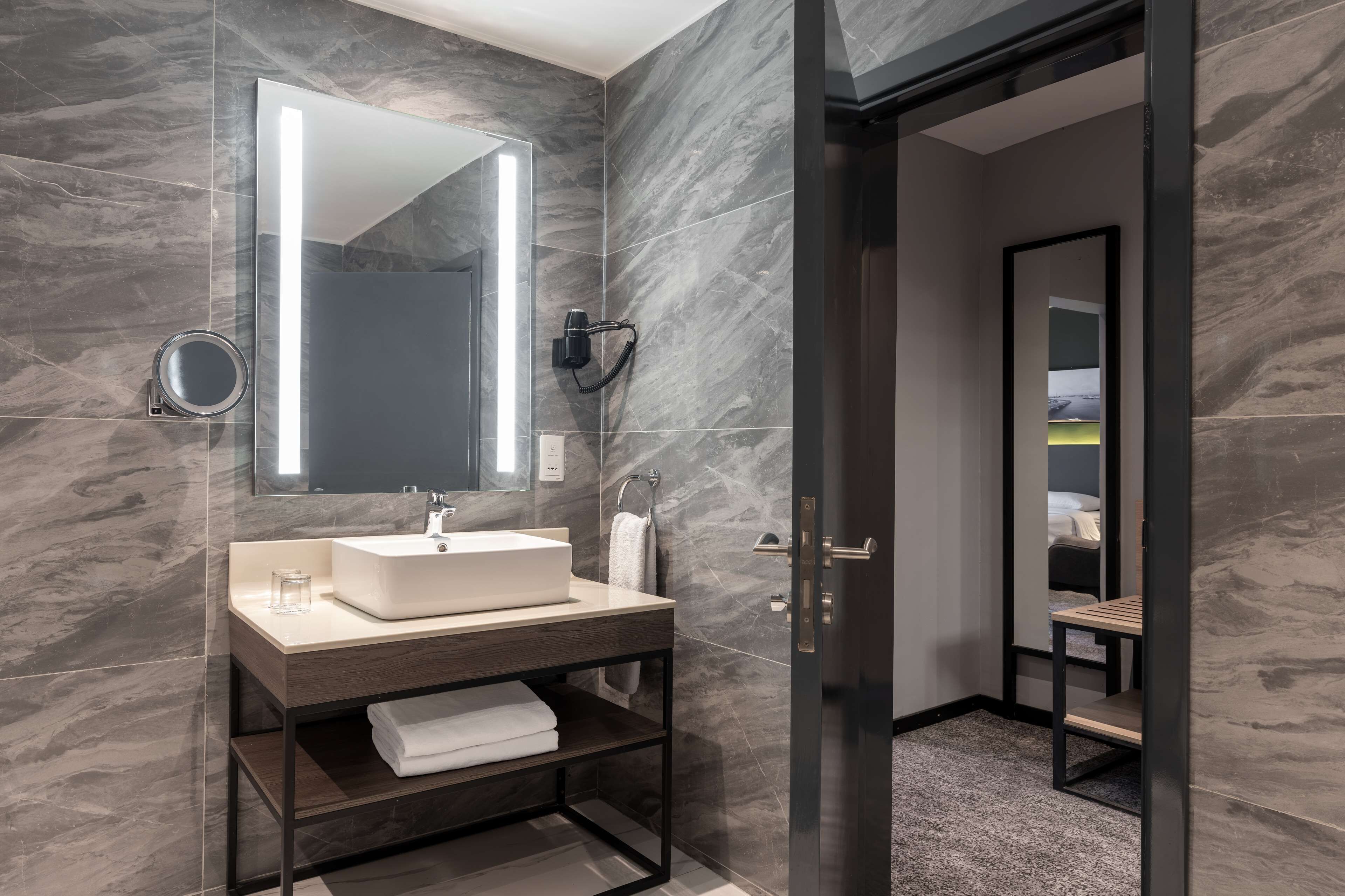 A modern bathroom with a marble wall, a large mirror, a sink, and a towel rack.