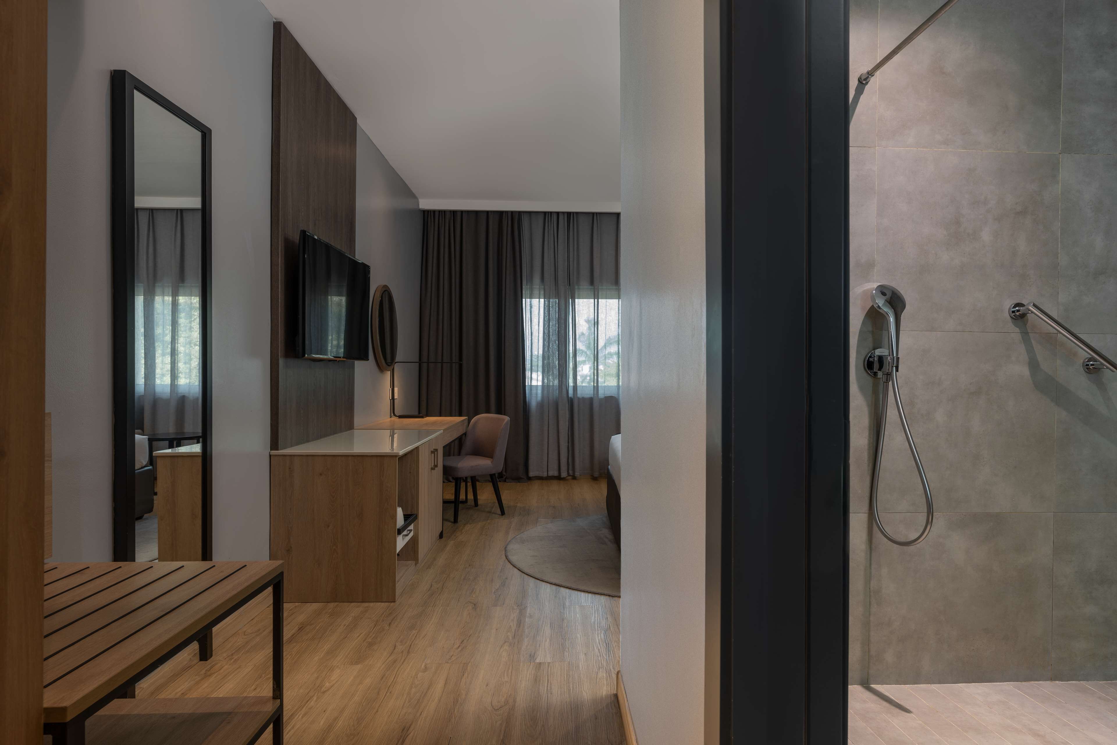 Een moderne hotelkamer met een houten bureau, een stoel, een televisie en een douche.