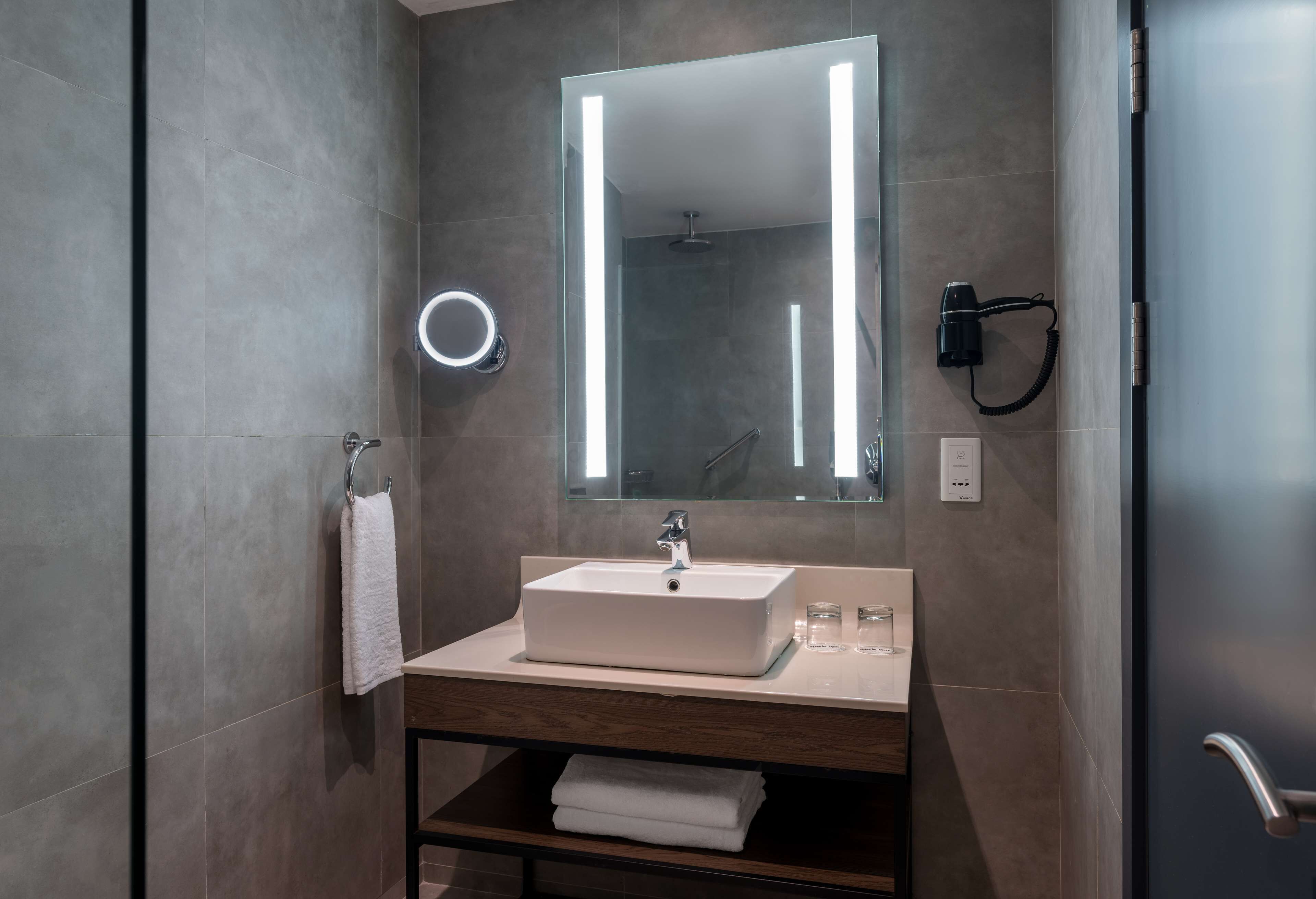 Un baño moderno con un lavabo rectangular, un espejo grande y un secador de pelo de mano.