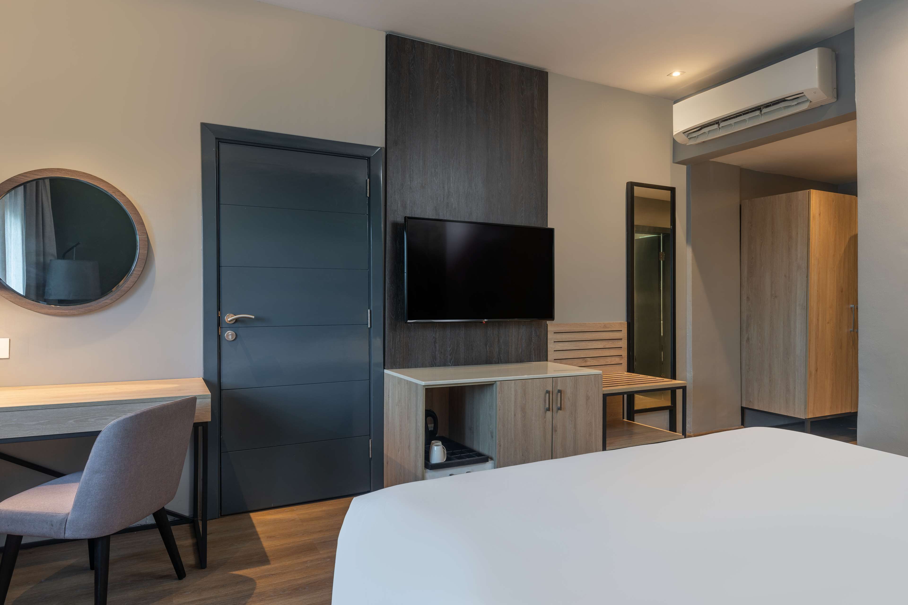 A modern hotel room with a bed, a desk, a chair, a TV, and a wardrobe.