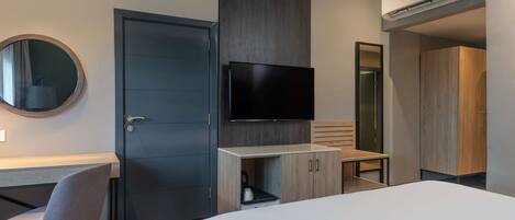 A modern hotel room with a bed, a desk, a chair, a TV, and a wardrobe.