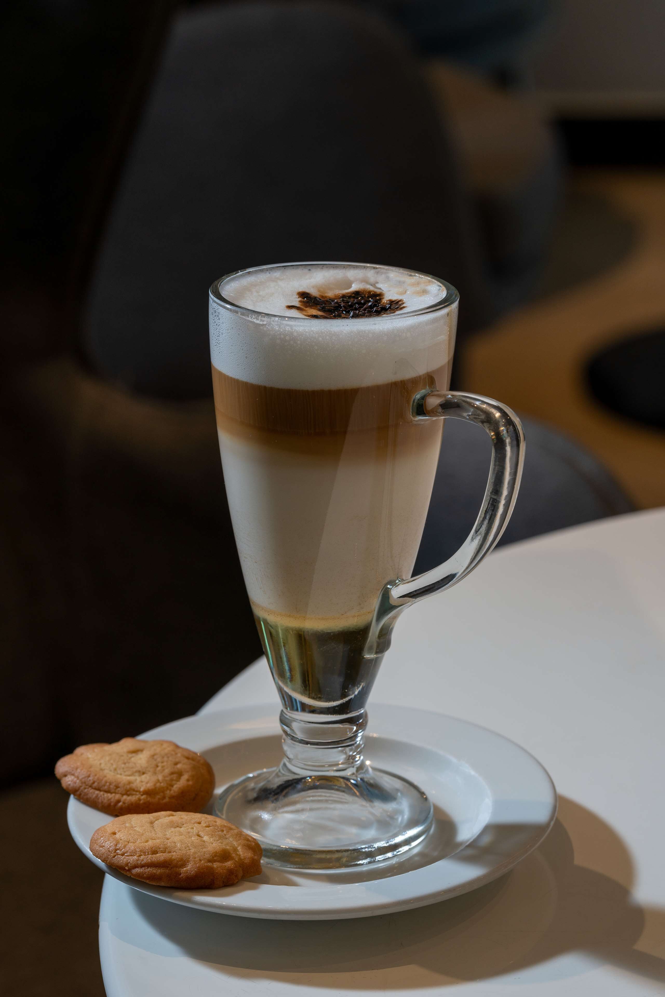 A tall glass of layered beverage with a handle, placed on a white plate with two cookies beside it.