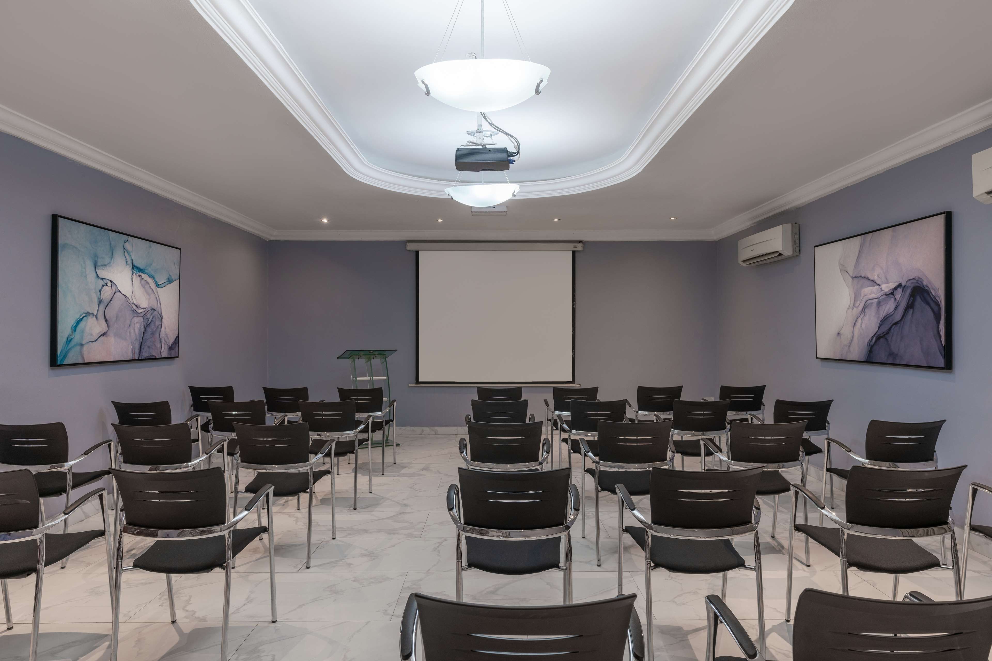 A conference room with rows of chairs, a projector screen, and abstract art on the walls.