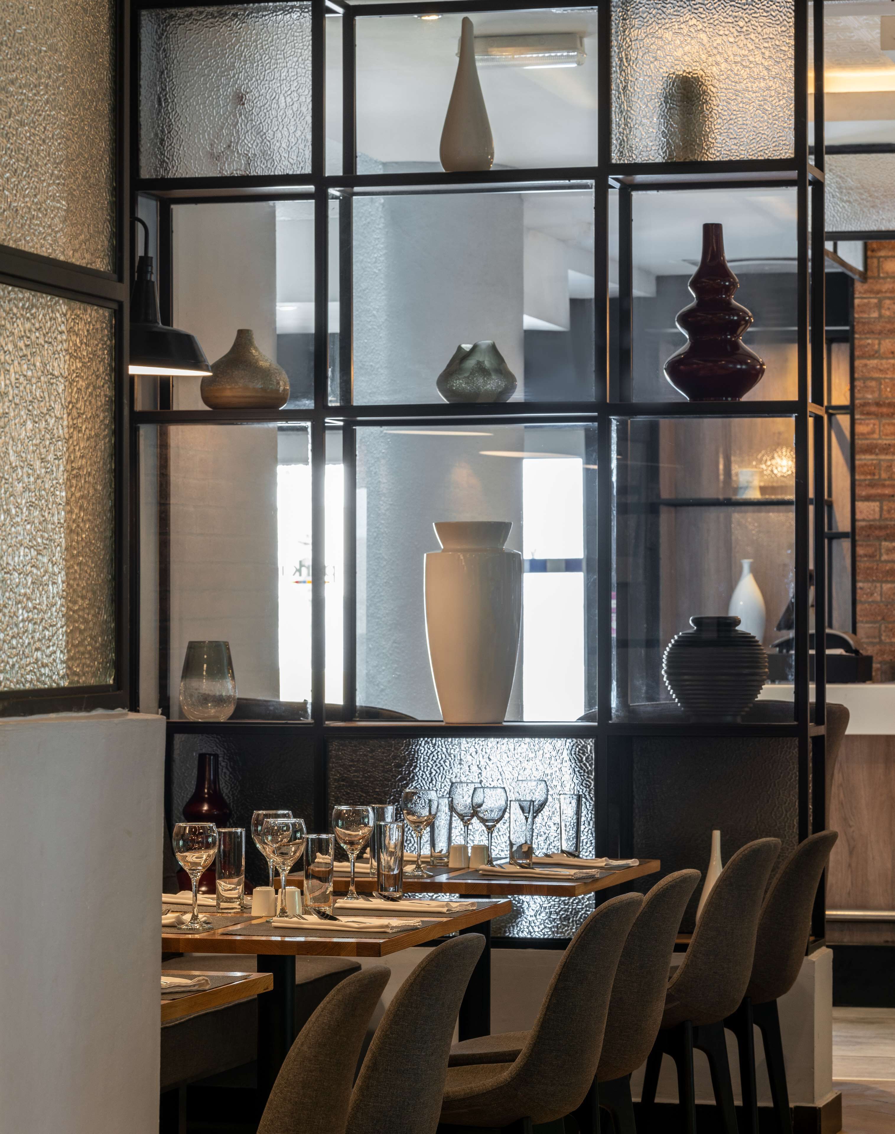 A dining area with a table set for six, surrounded by chairs, and a display of various vases behind a glass partition.