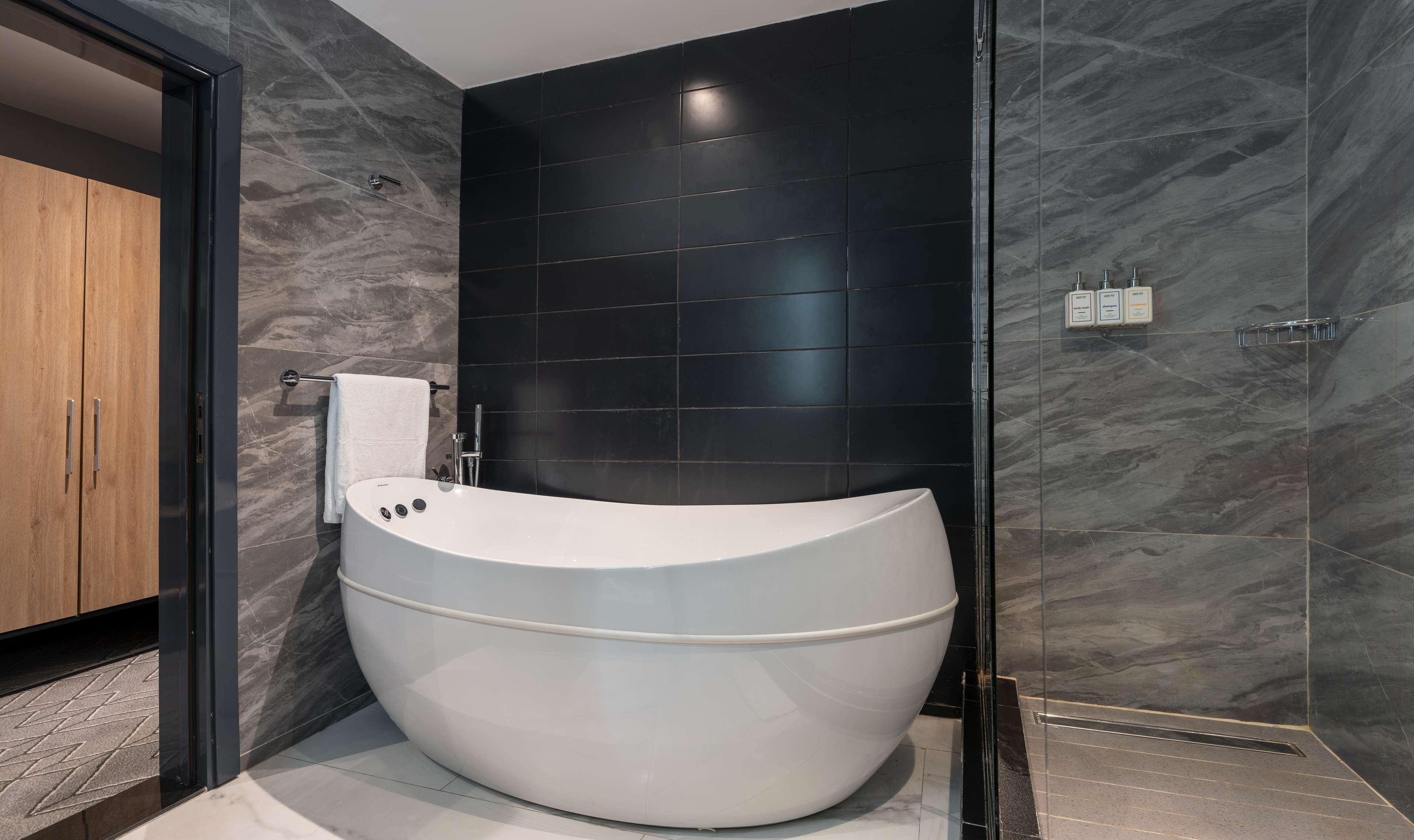 A modern bathroom with a freestanding bathtub, dark tiled walls, and a wooden cabinet.
