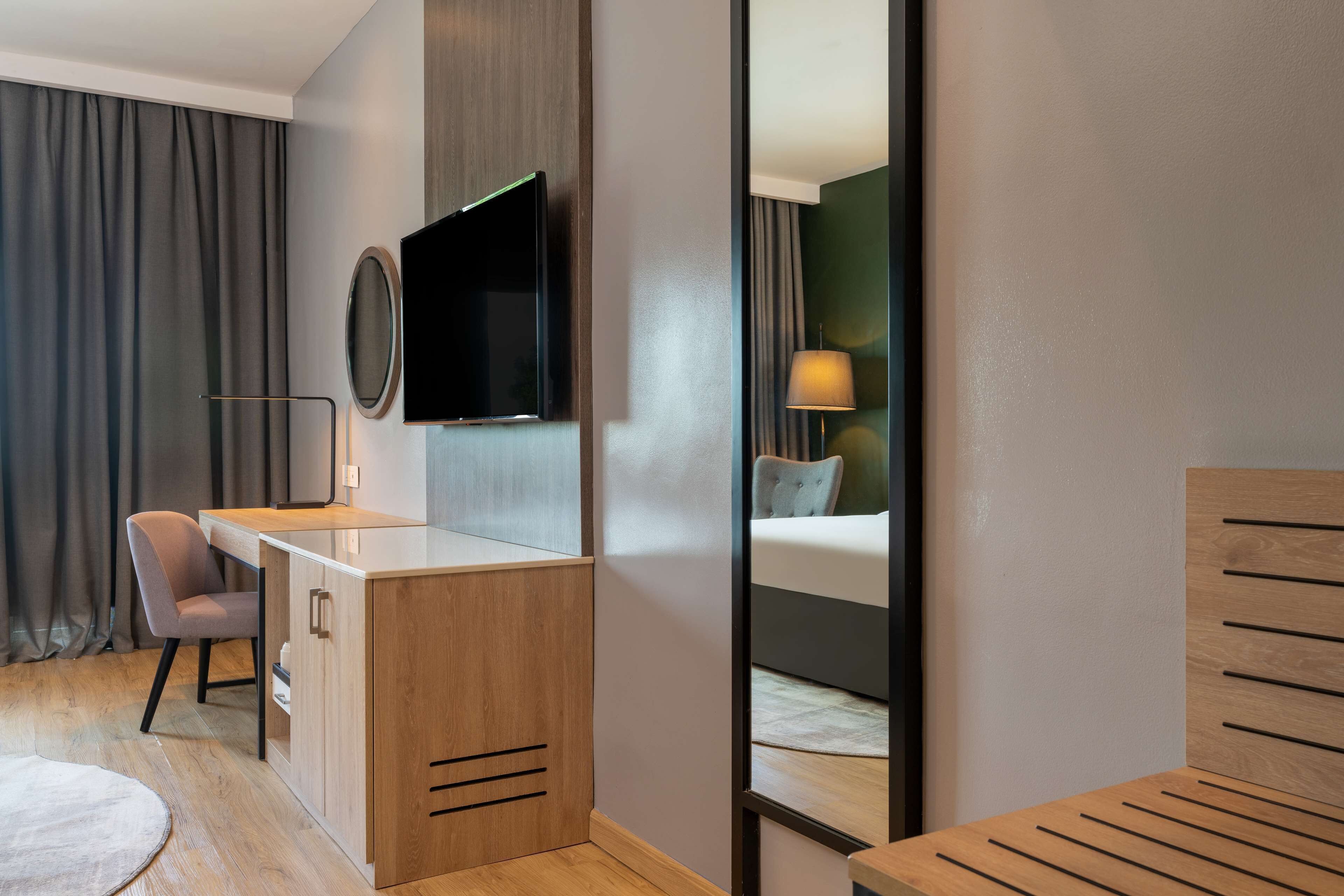Una habitación de hotel moderna con un escritorio de madera, un televisor de pantalla plana, una cama con cabecera y un espejo.