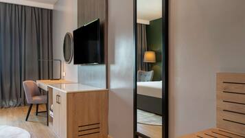 Una habitación de hotel moderna con un escritorio de madera, un televisor de pantalla plana, una cama con cabecera y un espejo.