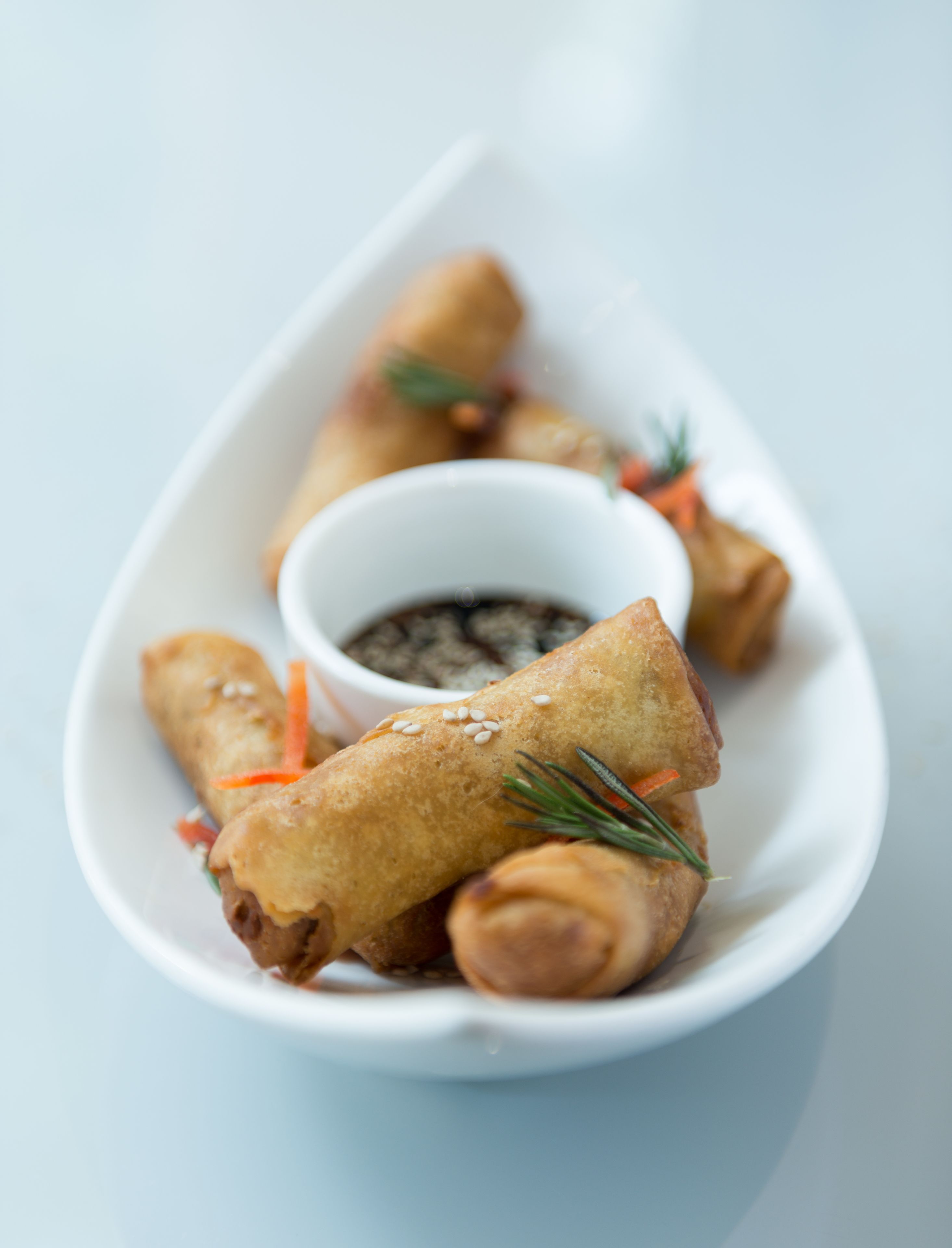 A white plate with spring rolls and a small bowl of dipping sauce.