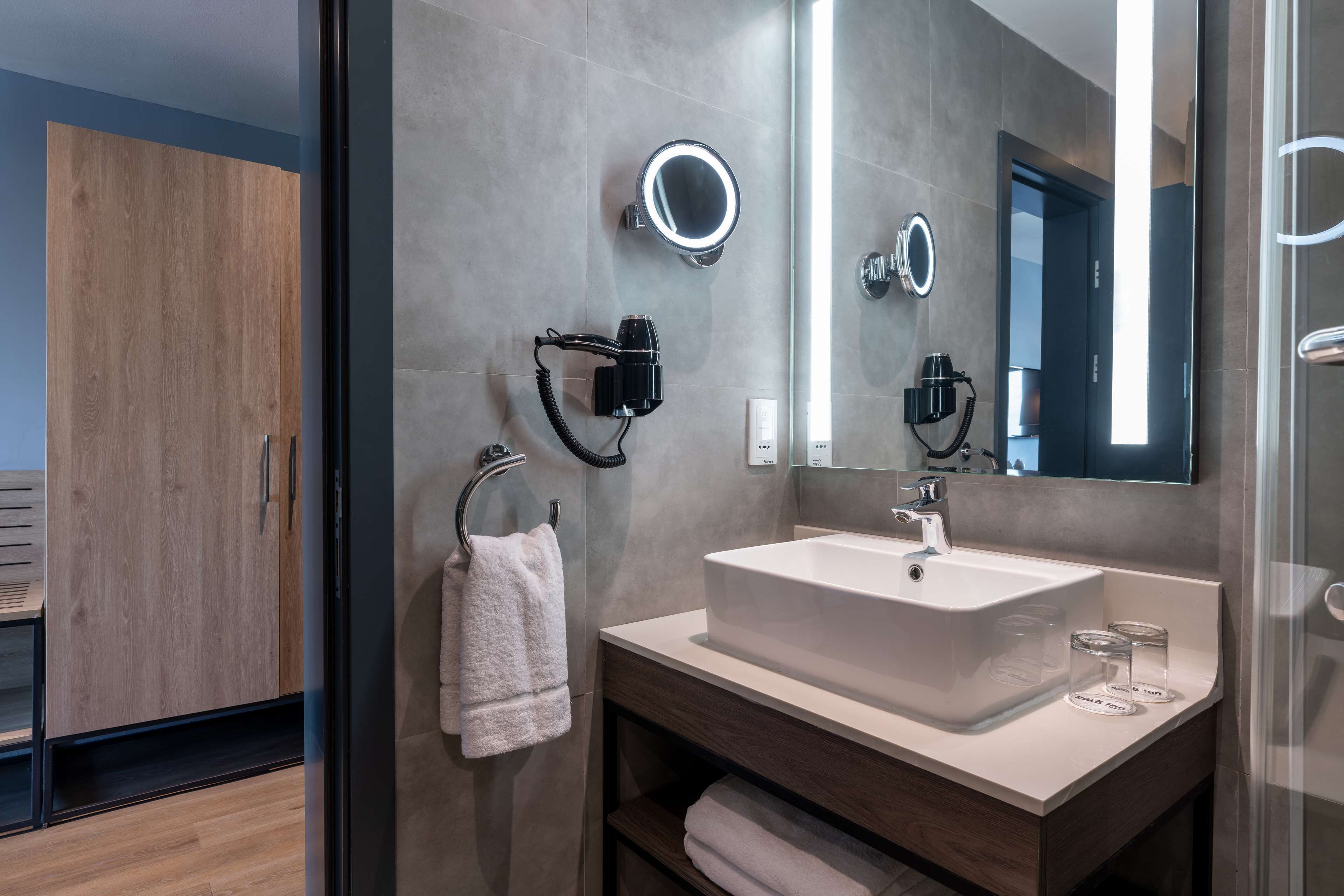 A modern bathroom with a large mirror, a white sink, and a towel rack.