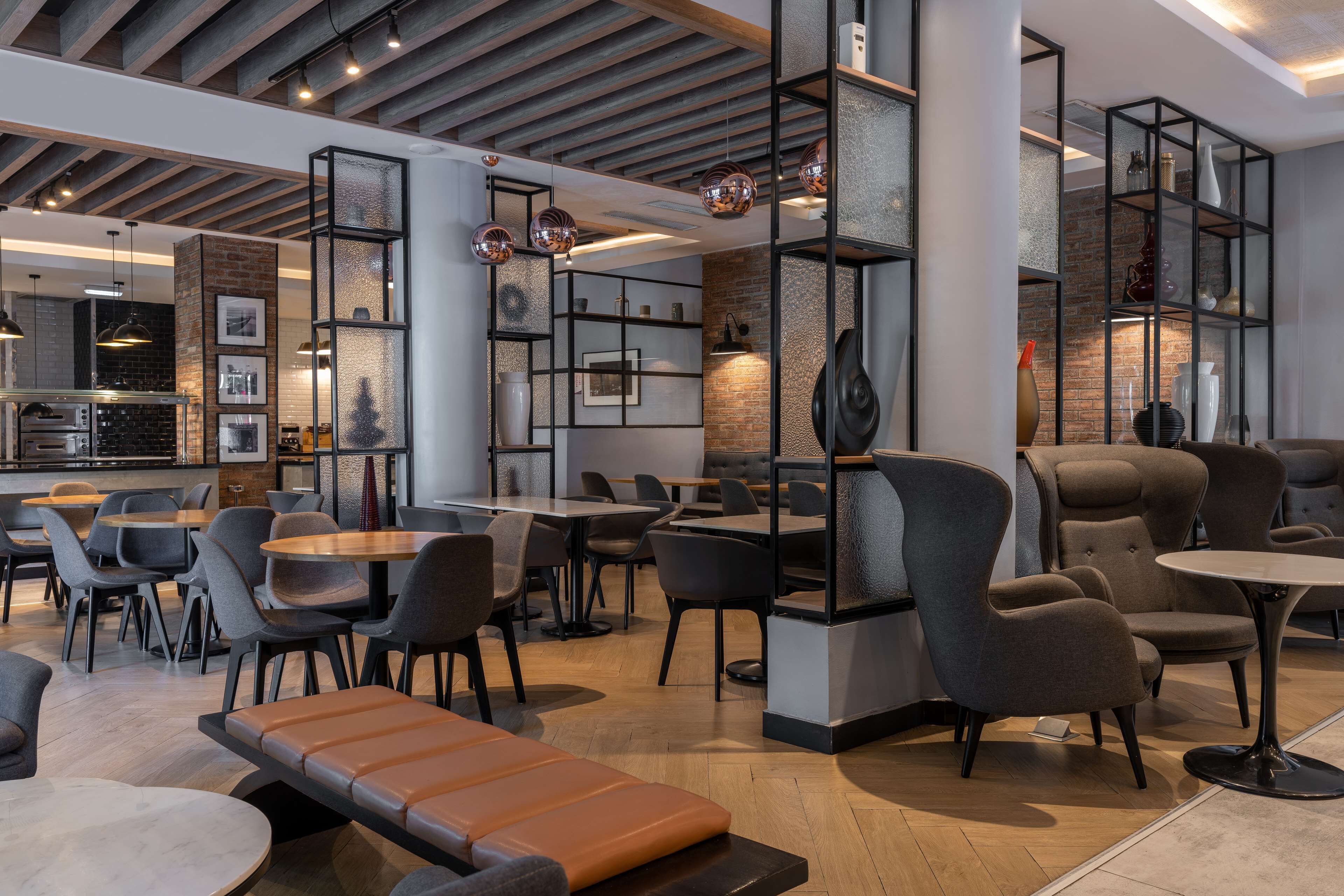 A modern cafe with wooden tables, cushioned seating, and exposed brick walls.
