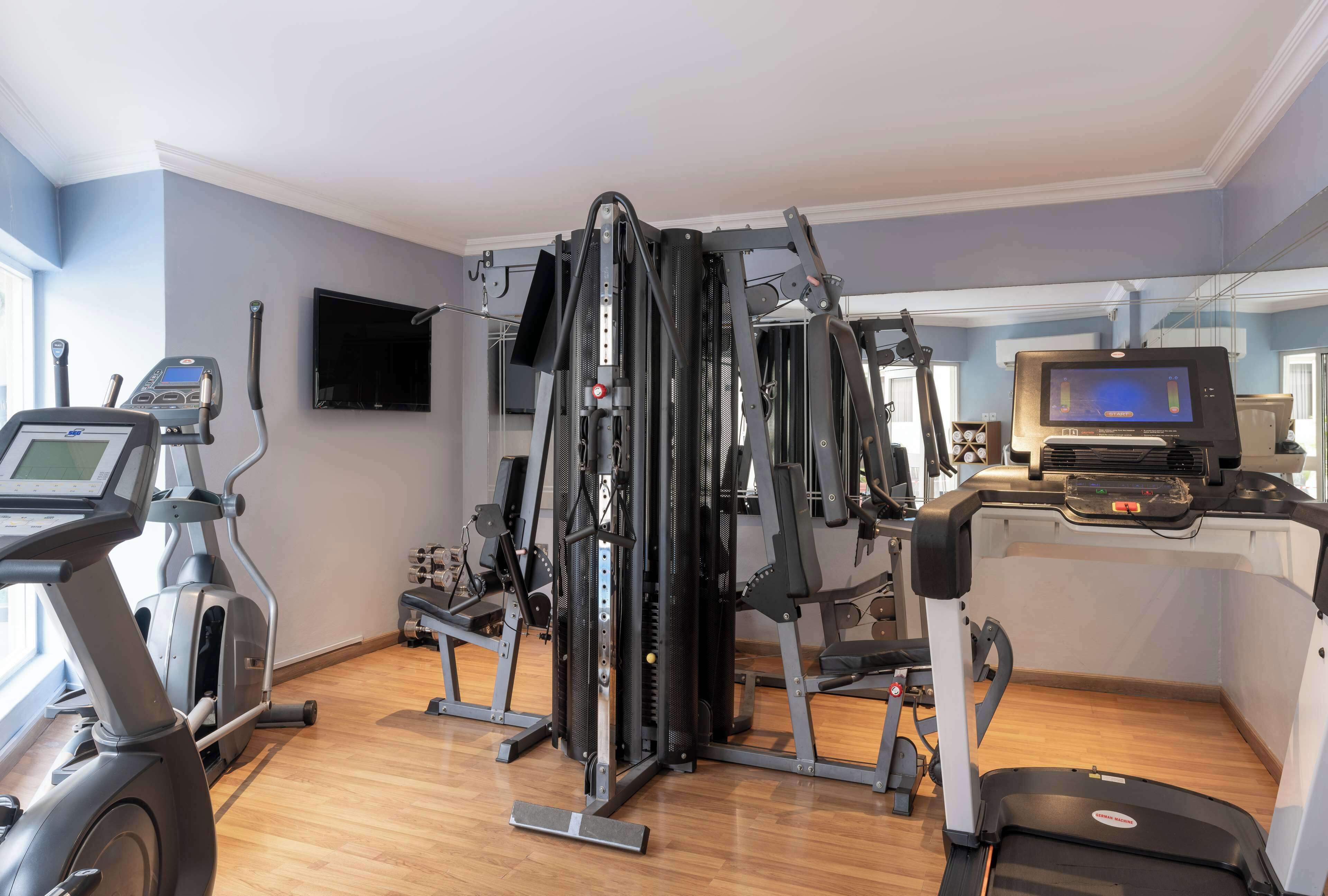 Un gimnasio con máquinas de cardio, equipo de entrenamiento de pesas y una pantalla de televisión.