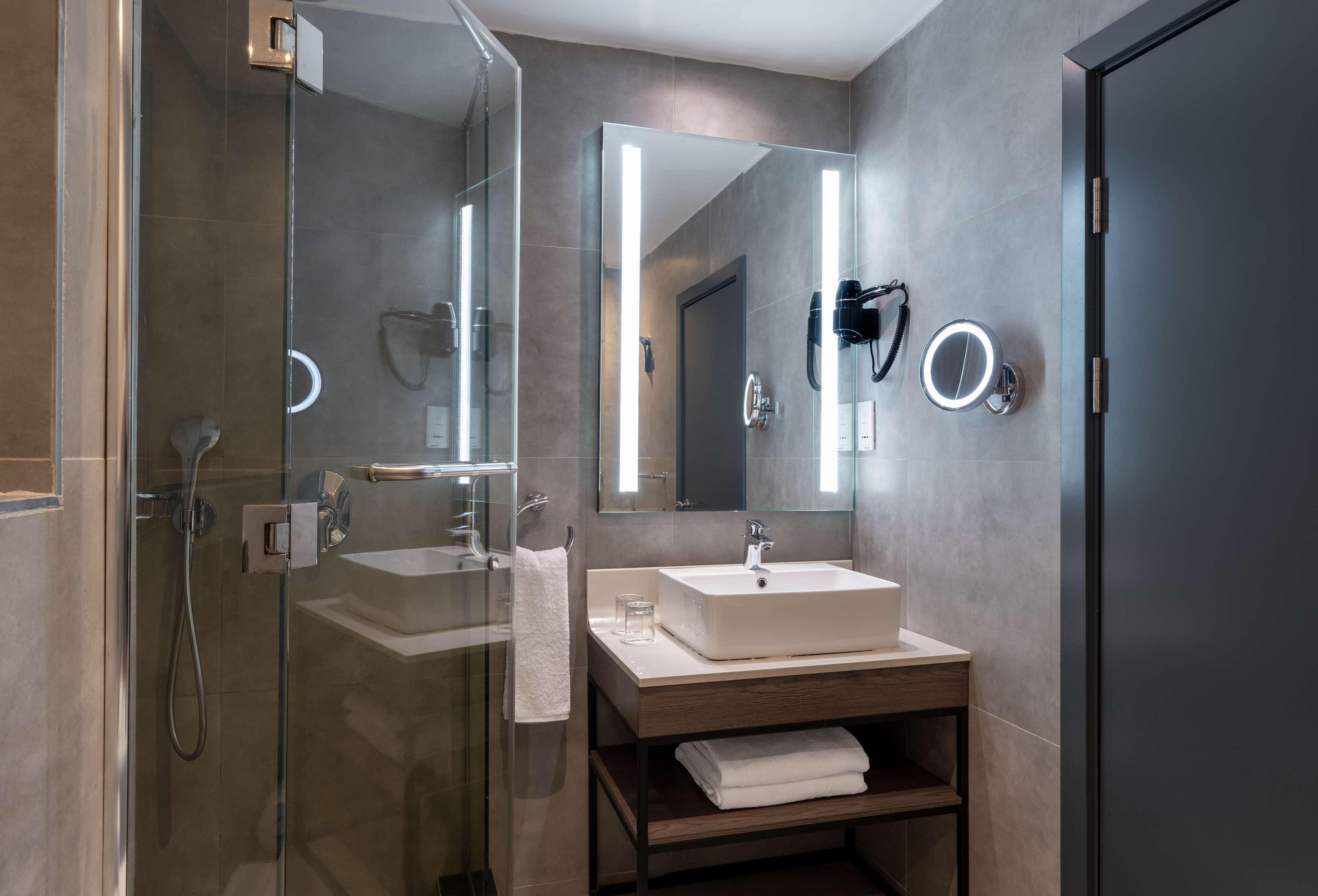 A modern bathroom with a glass-enclosed shower, a large mirror, and a vanity with a sink and towel rack.