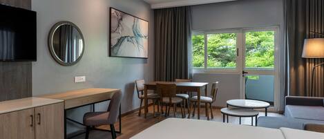 A modern hotel room with a bed, desk, chair, dining table, and a TV.