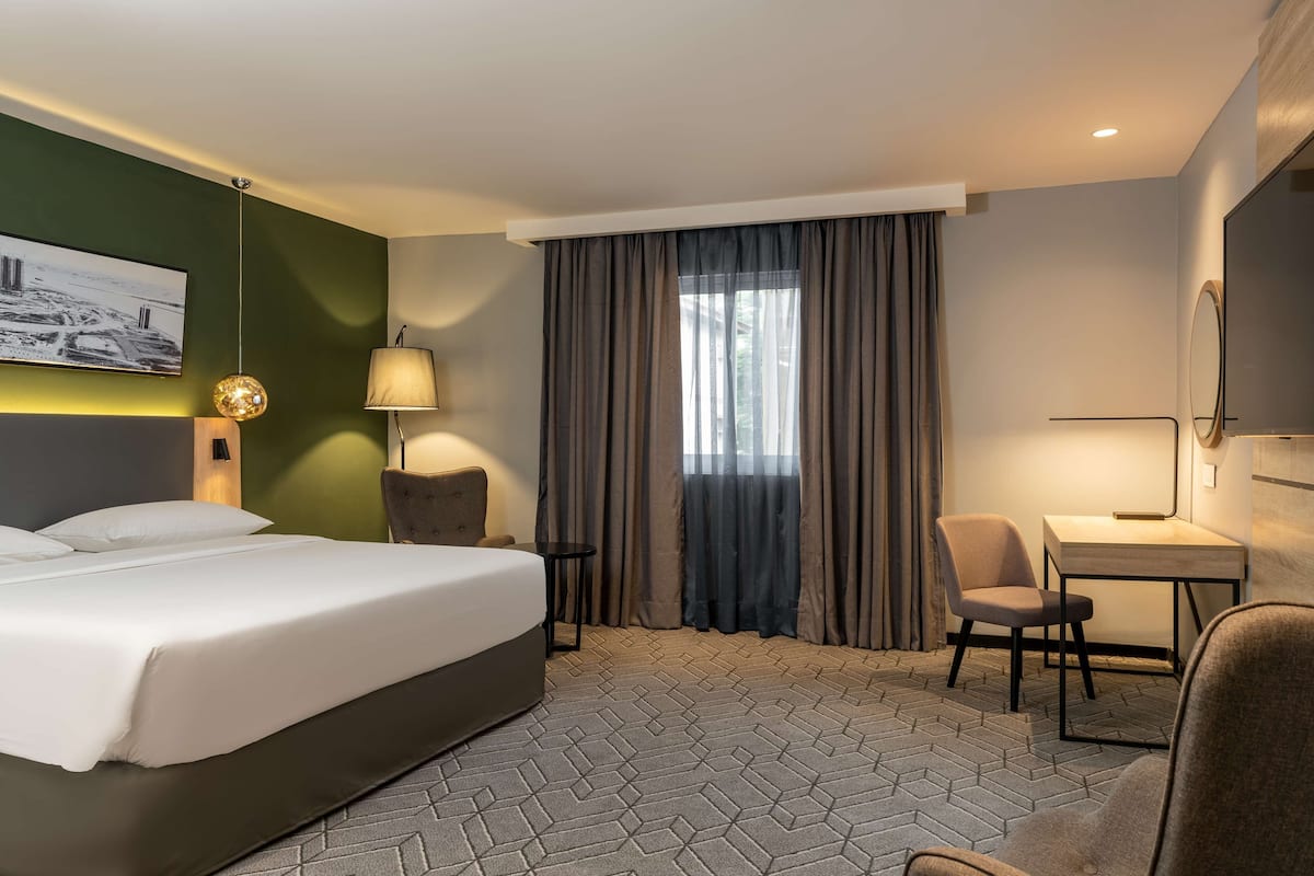 A hotel room with a bed, a desk, a chair, a lamp, and a painting on the wall.