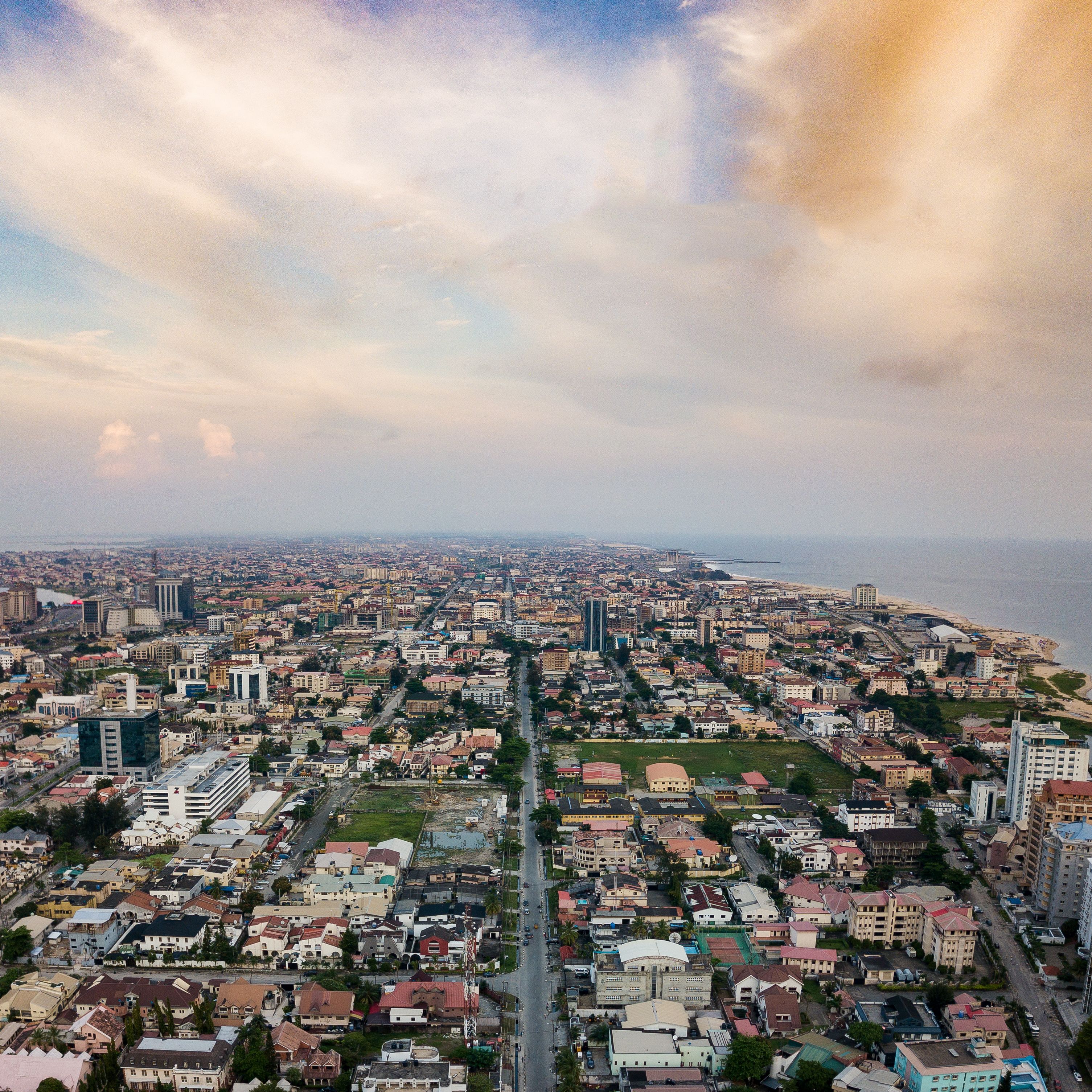 A cityscape with a mix of residential and commercial buildings, a prominent road, and a coastline in the distance.
