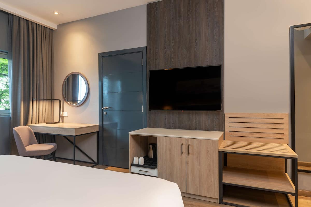 A modern hotel room with a bed, a desk, a chair, a TV, and a wardrobe.