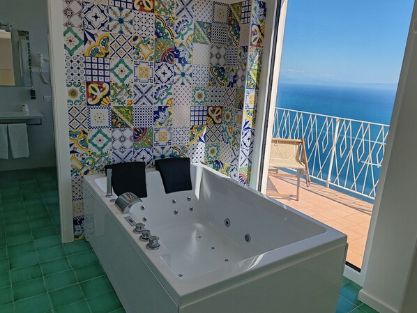 A bathroom with a large bathtub, a shower, and a toilet. There is a balcony with a view of the ocean.