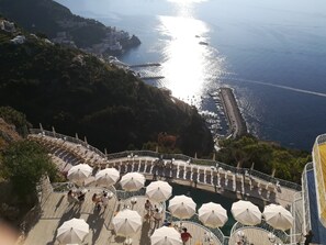 Une terrasse en bord de mer, agrémentée de parasols blancs et de tables, d’où l’on peut admirer une zone côtière avec des bâtiments et des bateaux.