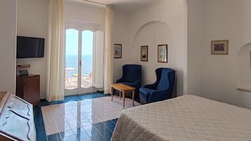 Habitación de hotel con cama, dos sillones, una mesita, televisión y balcón con vistas.