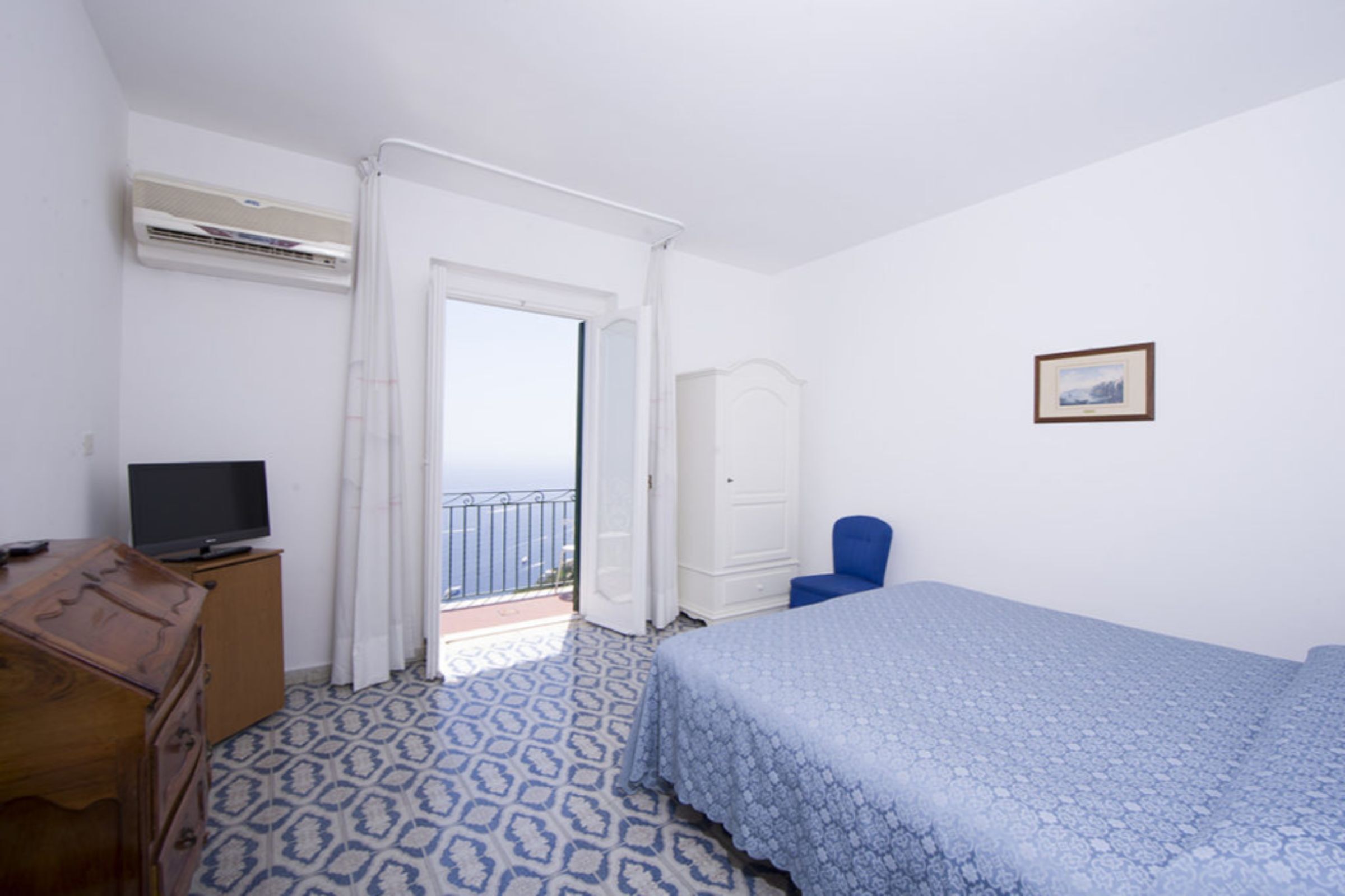 A bedroom with a bed, a television on a dresser, a wardrobe, and a chair.
