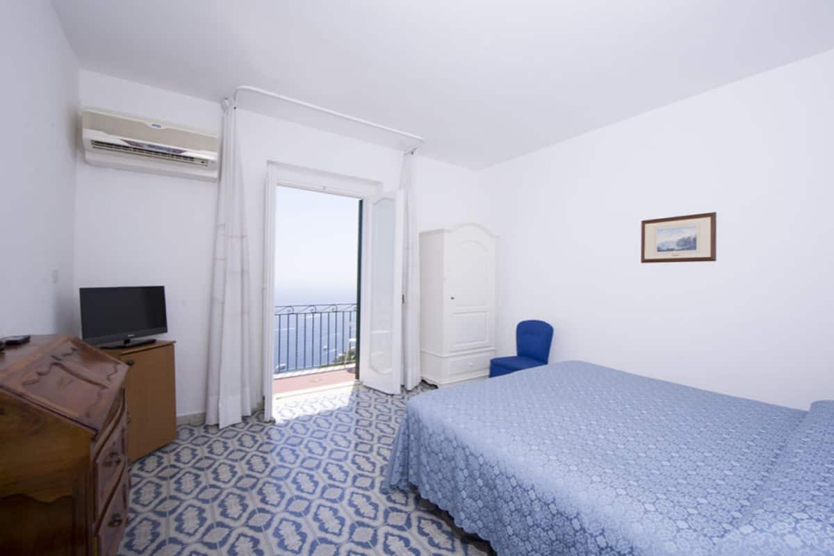 A bedroom with a bed, a television on a dresser, a wardrobe, and a chair.