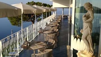 Eine Terrasse mit Sitzgelegenheiten im Freien, einer Statue und Blick auf das Meer.