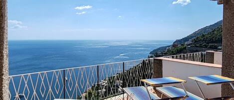 A terrace with a table and chairs, a view of the sea, and a tiled floor.