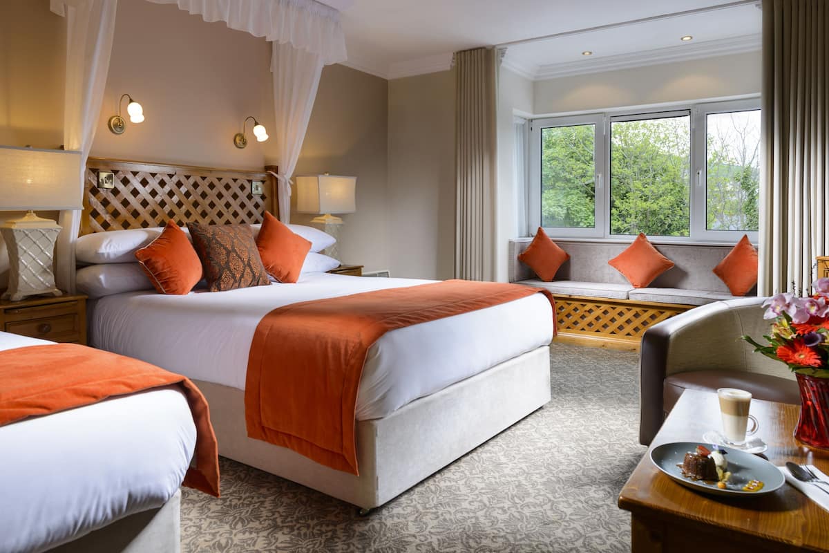 A hotel room with a large bed, a sofa, a dining table with a plate of food, and a window with a view of trees.