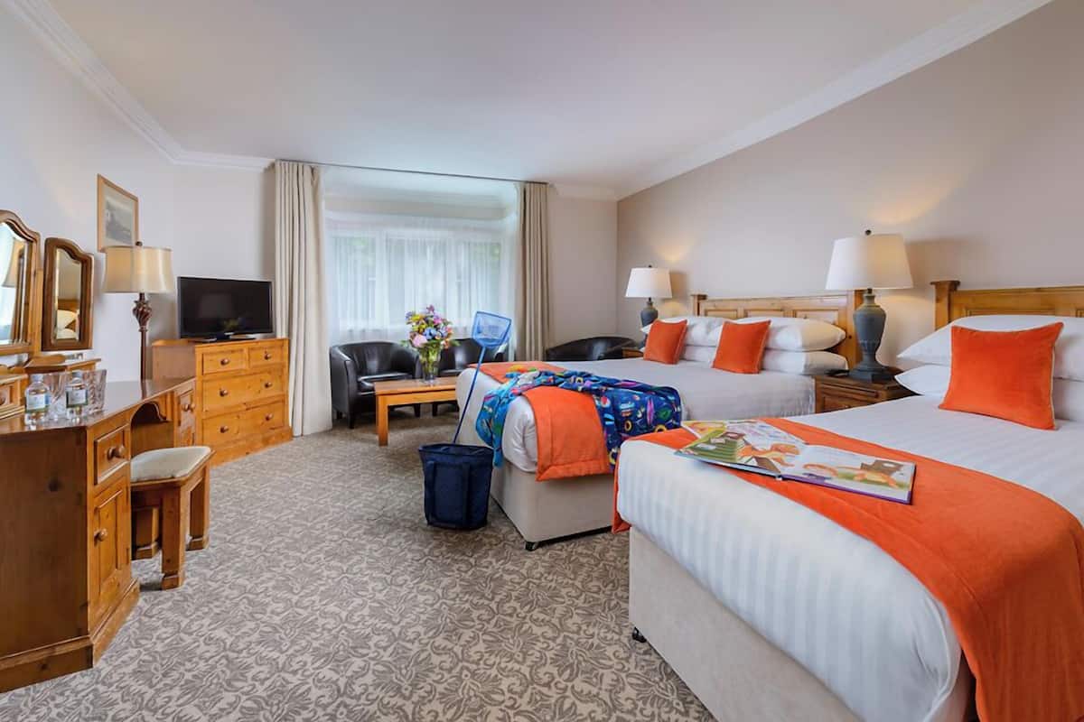 A hotel room with a large bed, two smaller beds, a desk with a TV, a chair, and a dresser.