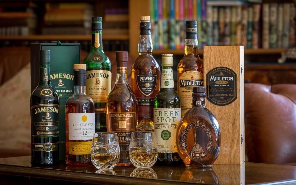 A selection of whiskey bottles and glasses on a wooden table with a leather couch in the background.