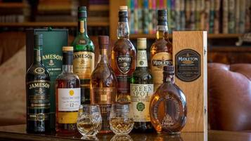 Várias garrafas de whisky e copos sobre uma mesa de madeira, com um sofá de couro ao fundo.