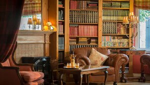 A cozy library with leather armchairs, a fireplace, and a large bookshelf filled with books. - Dingle Benners Hotel (Dingle)