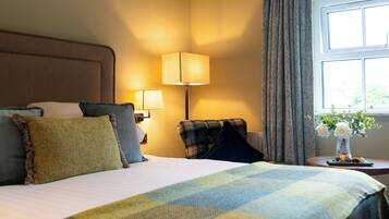 A hotel room with a bed, two bedside lamps, a chair, a small table with a vase of flowers, and a window with curtains.