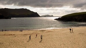 A beach with people walking and standing, surrounded by hills and the sea. - Dingle Benners Hotel (Dingle)