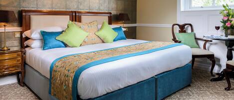 A neatly made bed with a blue and beige bedspread, a wooden headboard, and multiple pillows. There are two bedside lamps and a small table with a vase of flowers.