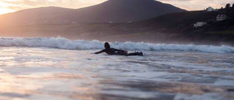 A person surfing on a beach with waves, a mountain in the background, and houses on the shore.