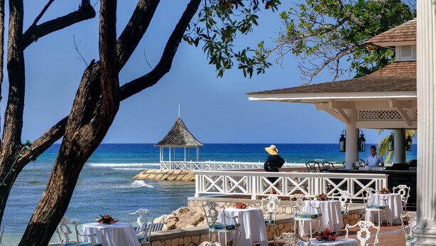 An outdoor dining area with tables and chairs, overlooking the ocean, and a gazebo in the background.