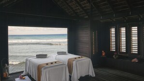 A room with two beds, a view of the ocean, and a wooden ceiling.