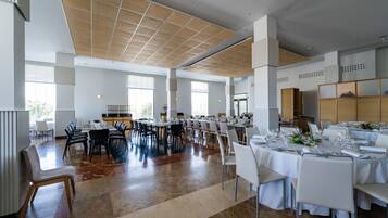 A spacious dining area with high ceilings and large windows, featuring multiple tables set for dining.