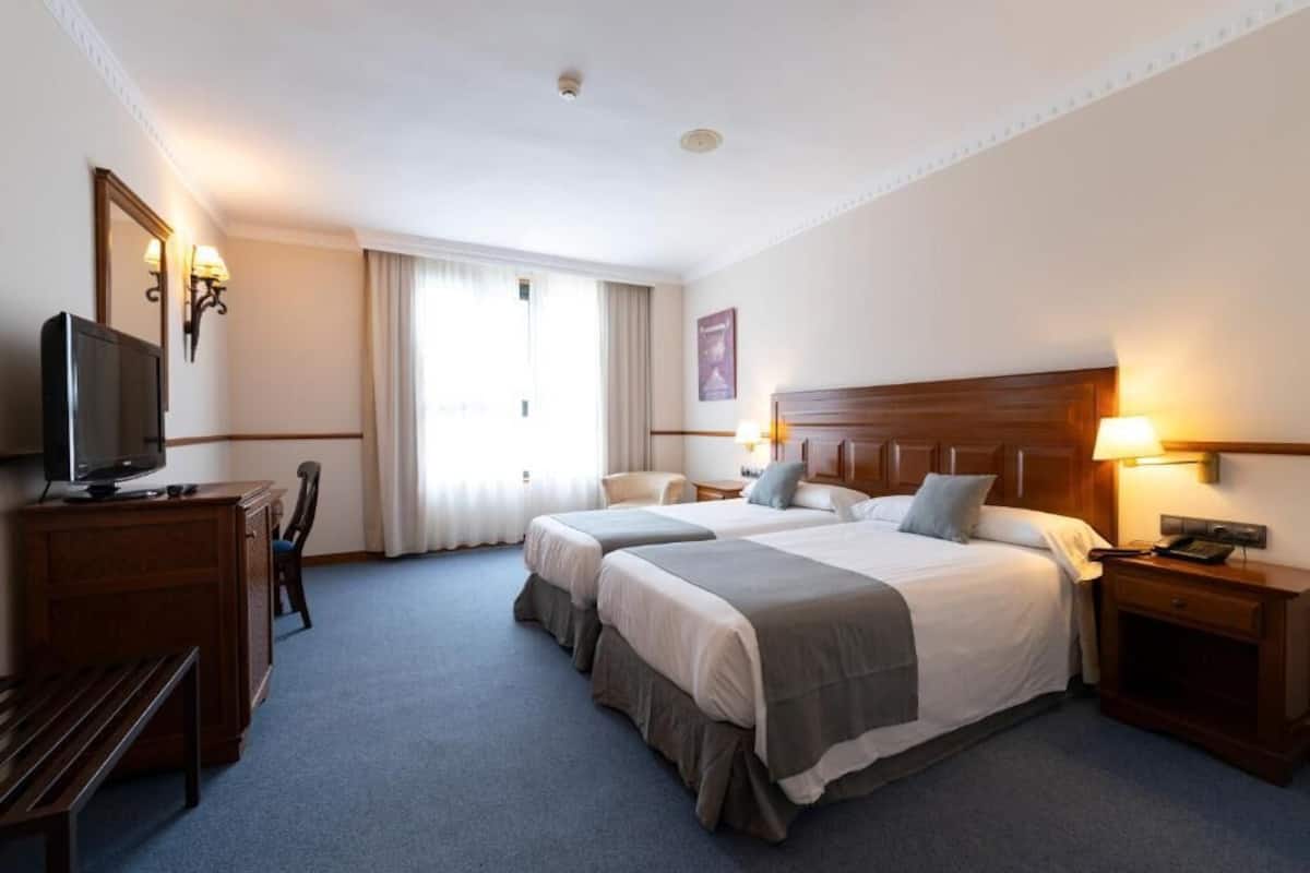 A hotel room with two beds, a TV, a desk, and a chair.