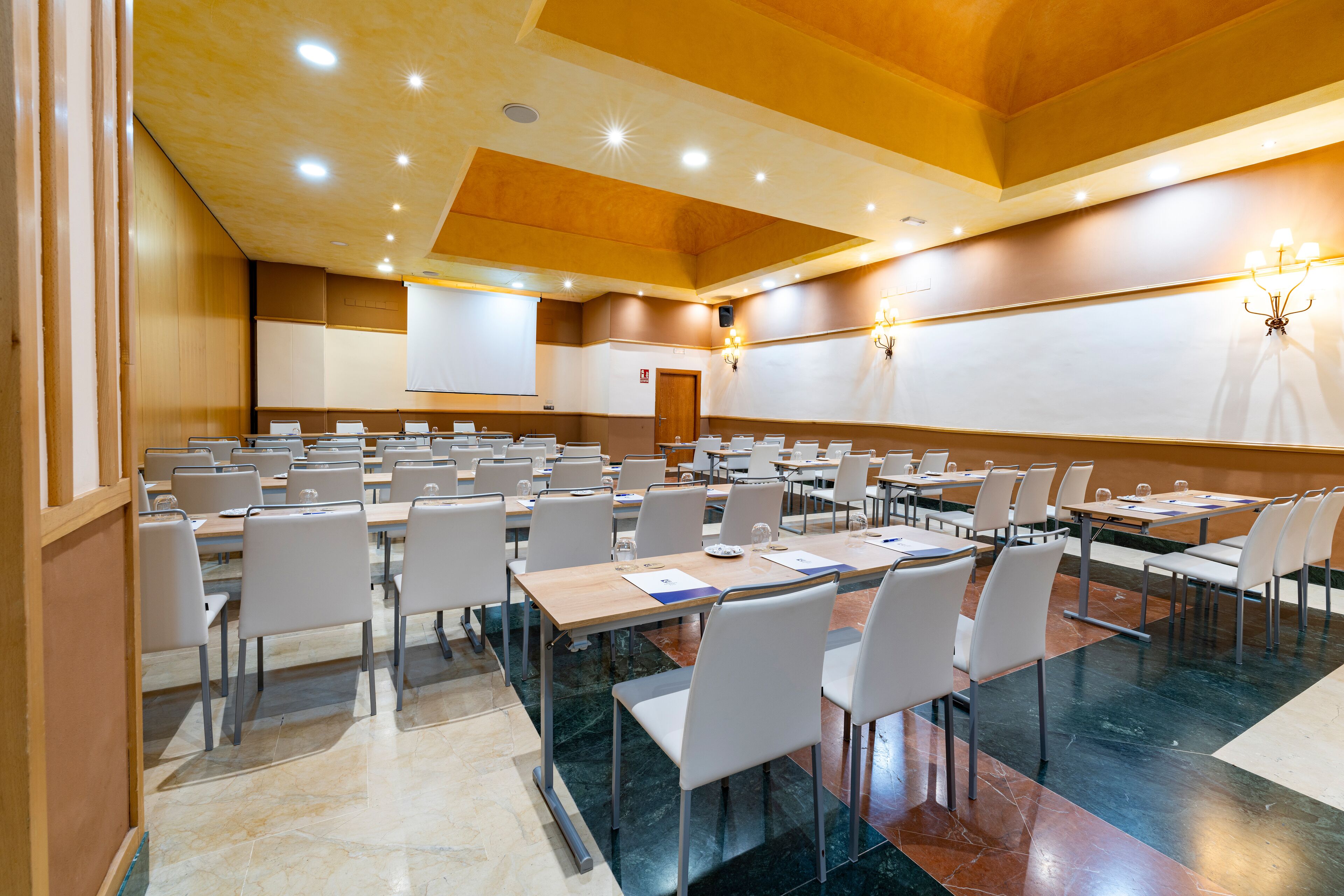 Una sala conferenze con diversi tavoli e sedie, uno schermo per proiettore e un lampadario.