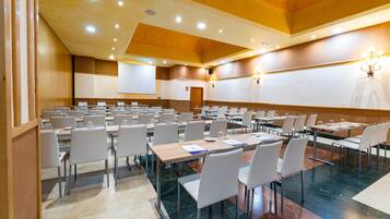 Una sala conferenze con diversi tavoli e sedie, uno schermo per proiettore e un lampadario.